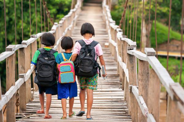 Three children with backpacks walking on a wooden bridge